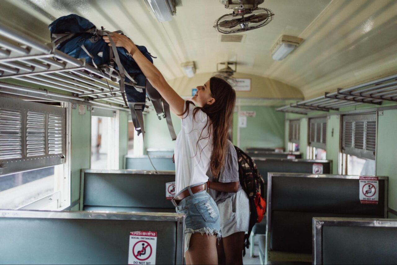 Girls on a train putting their bags on overhead shelf