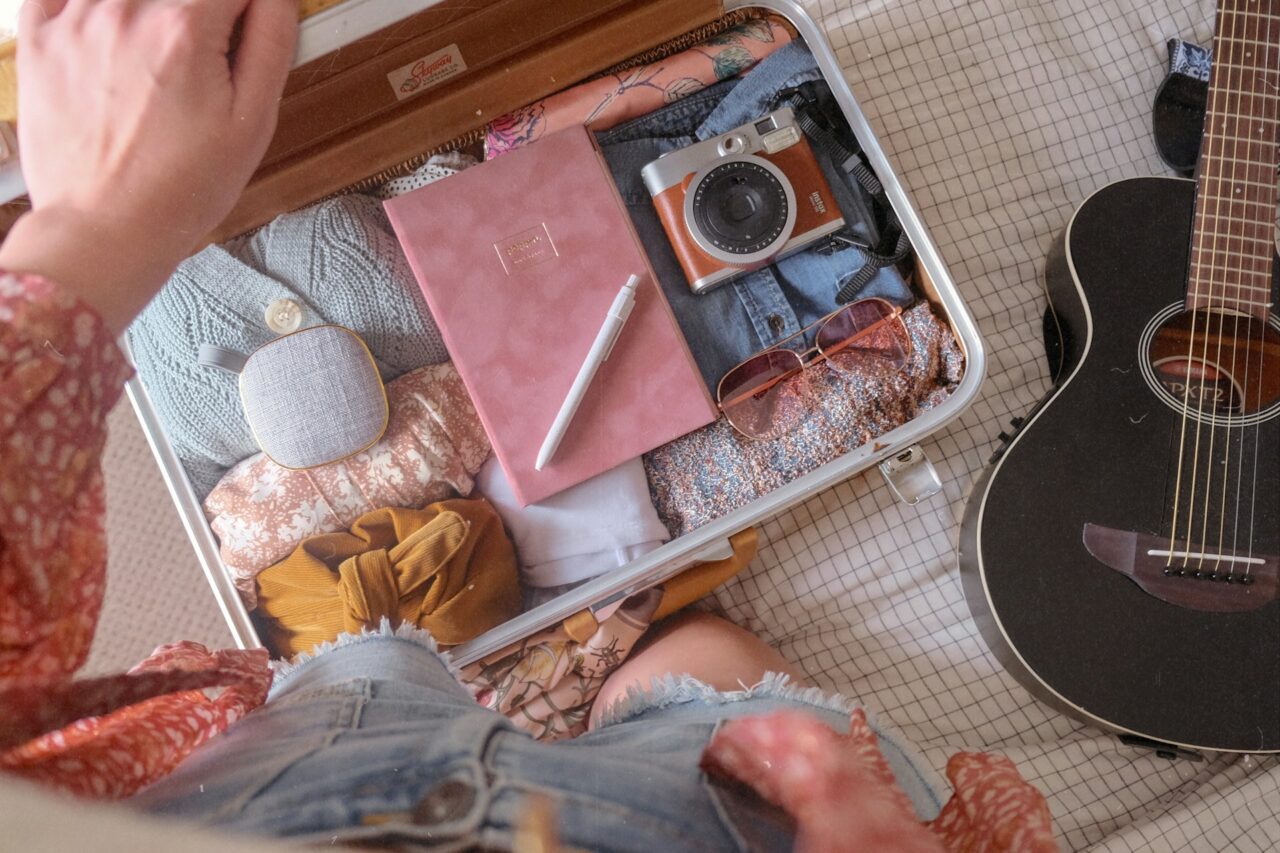 Woman packing a suitcase with clothes, camera and guitar on a bed