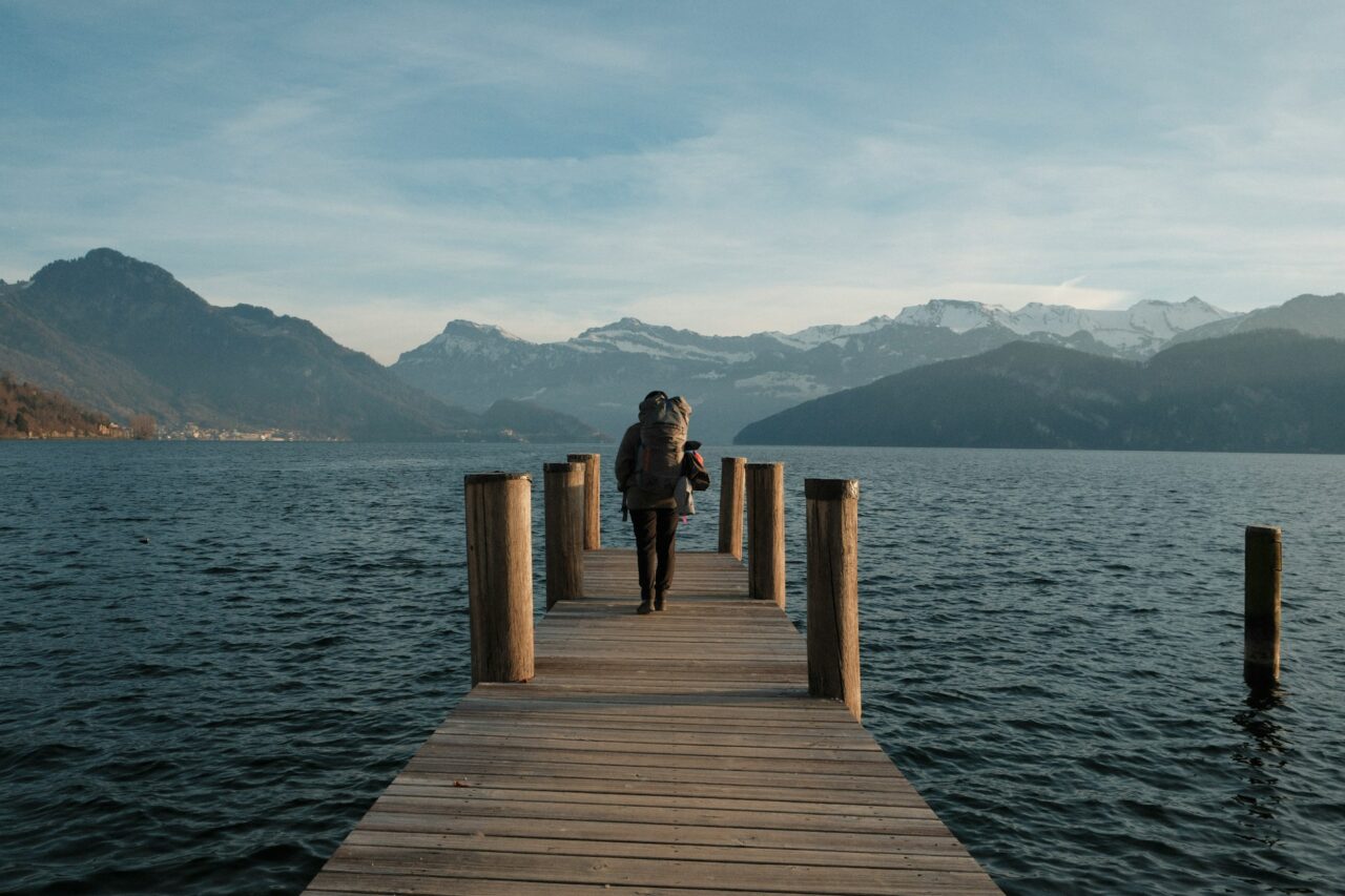 Person with a backpack standing on a jetty looking out at the water