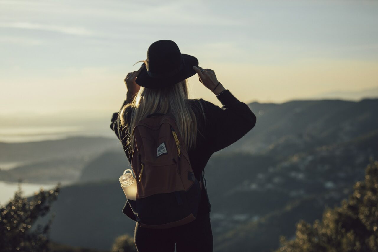 Solo female with a backpack and hat looking out at a view